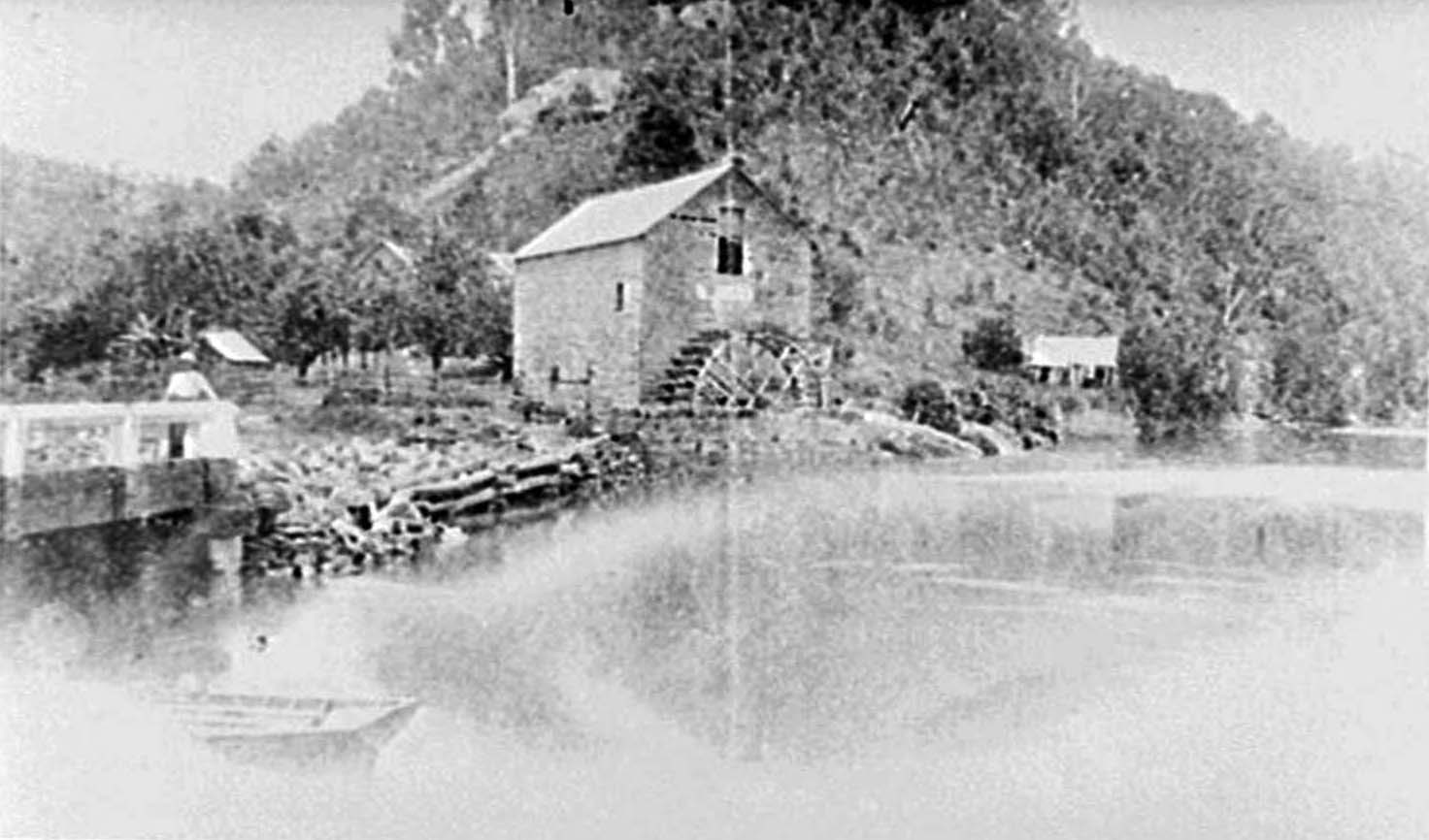 A photograph showing Singletons Flour Mill and the boat house at Laybury Creek, Wisemans Ferry NSW. Detail of the crib construction of the mill wall is shown.